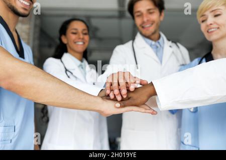 Lavoro di squadra, concetto di cooperazione. Motivato gruppo multietnico amichevole di medici professionisti uomini e donne in abbigliamento da lavoro che si acclamano, mettendo le mani sulla parte superiore Foto Stock