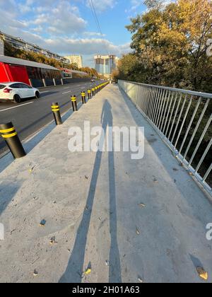 Colpo verticale di silhouette femminile sul marciapiede con paletti di sicurezza neri sul lato Foto Stock