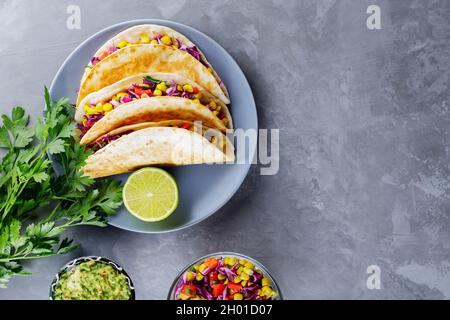 Tacos messicani con verdure e guacamole su sfondo grigio. Tacos vegani con mais, cavolo viola e pomodori su un piatto grigio. Spazio di copia. Top vi Foto Stock