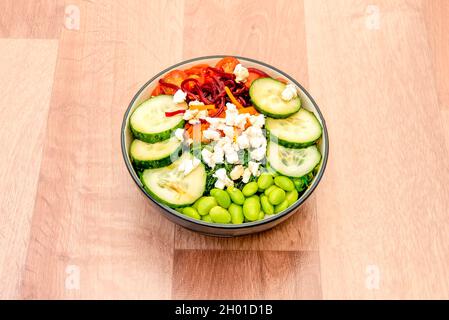 Recipiente vegano con fette di cetriolo, fagioli di edamame, pomodori ciliegini, riso bianco, insalata di alghe di wakame, carota grattugiata e barbabietola Foto Stock