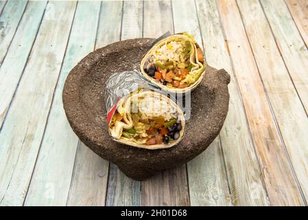 Burrito vegetale gigante, riso bianco, fagioli neri e guacamole su pietra vulcanica messicana molcajete su tavola di legno Foto Stock