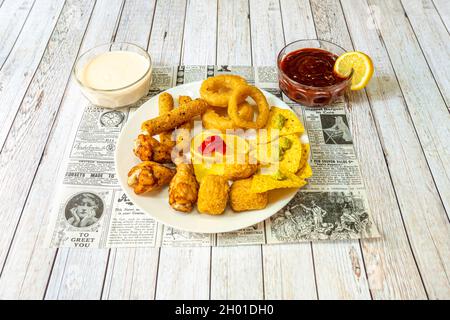 Piatto con antipasti messicani e texani assortiti, pepite di pollo fritte, anelli di cipolla, bastoncini di mozzarella e salsa barbecue con patatine di mais Foto Stock