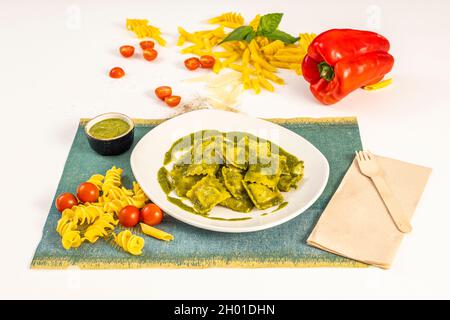 Piatto di ravioli ripieni di carne con salsa di pesto, pasta fresca, pomodori ciliegini e peperoni rossi e pomodori ciliegini Foto Stock