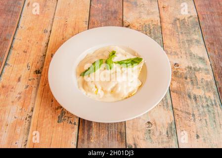 Ravioli ripieni di formaggio ricoperto di besciamella e foglie di basilico su tavola di legno Foto Stock