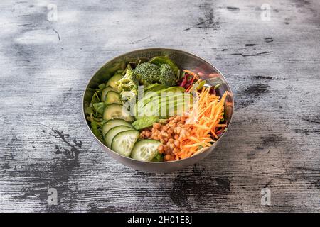 Ciotola vegana con pezzi di cetriolo, spinaci di broccoli, carote grattugiate e barbabietole, rucola e spinaci, lenticchie stufate e avocado maturo Foto Stock