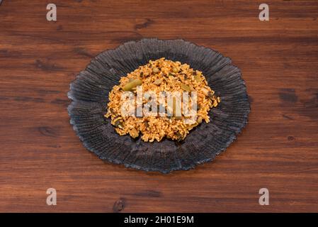 Razione di paella di riso con verdure e funghi servita su un bel piatto di vetro nero su un tavolo di legno Foto Stock