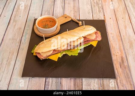 Panino di pastrami con patate cotte a fette, formaggio cheddar, lattuga e pomodoro spalmato sul pane Foto Stock