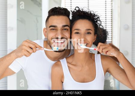 Ritratto di giovane coppia allegra Medio Oriente spazzolando insieme i denti e sorridendo a Camera, felice coniugi arabi tenendo spazzolini da denti, godendo Maki Foto Stock