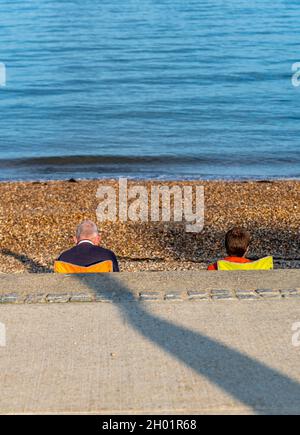 vista inconsueta di una coppia più anziana seduta su una spiaggia sul mare sull'isola di wight. vista testa e spalle di una coppia anziana sulla spiaggia. diverso. Foto Stock