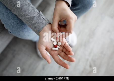 Cropped infelice donna europea depressa millennial tenere molte pillole in mano e pensare al suicidio, vista dall'alto, spazio libero. Molti problemi, esagerare Foto Stock