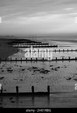 Immagine bianca e nera di groynes di legno che serve come seadefenses sulla spiaggia di Bognor Regis. Foto Stock