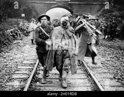 Un prigioniero tedesco, ferito e fangoso, aiutato da un soldato britannico lungo una pista ferroviaria. Foto Stock