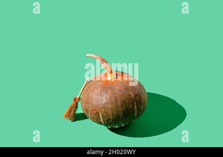 Una bella zucca marrone e arancione e una scopa appoggiata su di essa. Sfondo verde pastello. Concetto creativo minimo di Halloween e Thanksgiving. Foto Stock