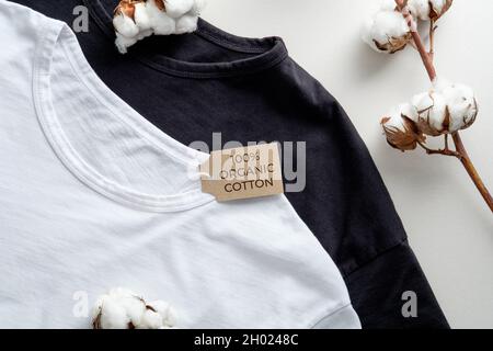 T-shirt in cotone naturale biologico e fiori di piante di cotone su tavola bianca. Abbigliamento ecologico, moda, concetto di stile di vita sostenibile Foto Stock