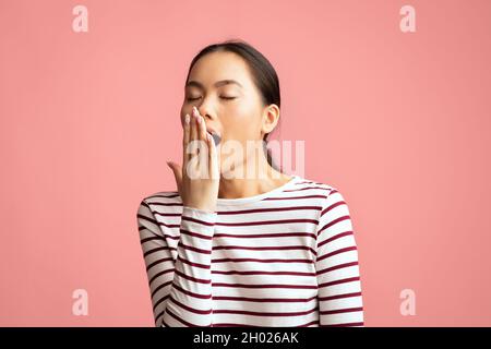 Closeup shot di giovane donna asiatica stanca yawning, annoiato femmina coreana indifferente che copre bocca aperta con la mano, sensazione di esausto e sonnolento mentre s Foto Stock