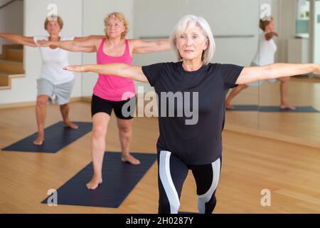 Donna anziana in piedi in affondo asana Virabhadrasana in studio yoga Foto Stock