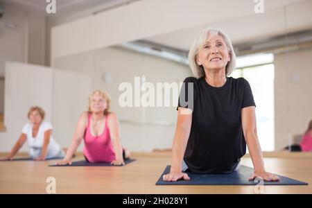 Donna matura sorridente che fa verso l'alto cane che si allunga posa in studio yoga Foto Stock