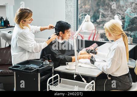 Il maschio utilizza lo smartphone durante le procedure di bellezza Foto Stock