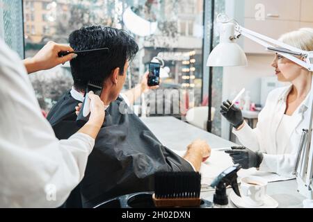 Visitatore del salone di bellezza fotografando mentre si ottiene il taglio dei capelli Foto Stock