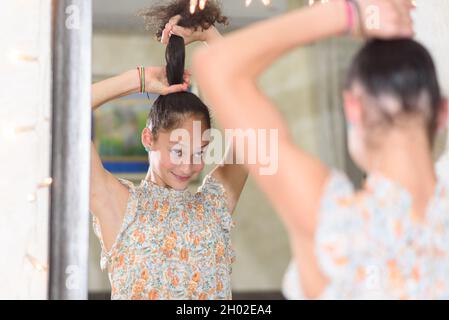 Vista posteriore della ragazza teen che guarda lo specchio e che fa un ponytail. Foto Stock