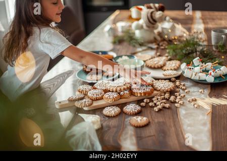 La ragazza carina decora il pan di zenzero con la glassa dello zucchero. Preparazione per il concetto di Natale. Foto Stock