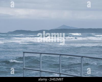 Un uccello gabbiano d'Argento australiano che vola attraverso un cielo blu luminoso con alcune nuvole bianche e grigie fluffy, Australia Foto Stock