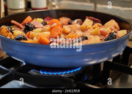 Patate, carote, prosciutto e aglio nero sono fritte in padella Foto Stock