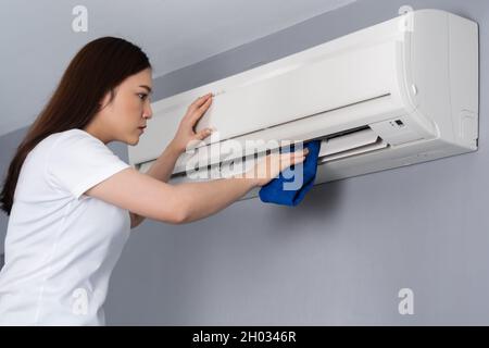 giovane donna che pulisce il condizionatore d'aria con un panno a casa Foto Stock