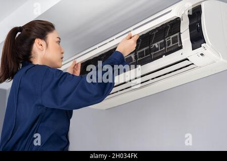 intervento tecnico femminile aprire l'interno dell'impianto di climatizzazione per il controllo e la riparazione Foto Stock