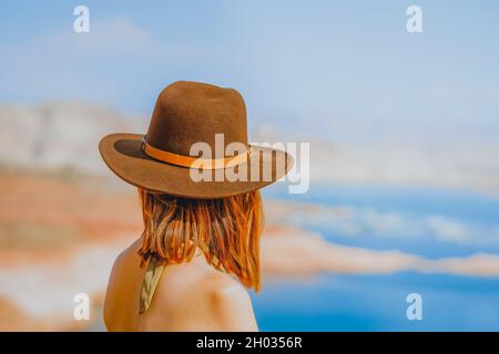 Donna dai capelli rossi che indossa un cappello sulla spiaggia che si affaccia sul lago, vista posteriore Foto Stock