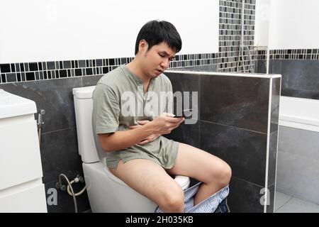 uomo infelice con stomachache usando lo smartphone e seduto nel water ciotola in bagno a casa Foto Stock