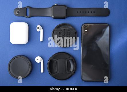 Foto di auricolari senza fili, coperchi per obiettivi della fotocamera, telefono cellulare e smart watch su sfondo blu Foto Stock