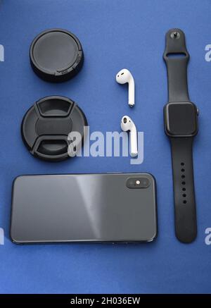 Foto di auricolari senza fili, coperchi per obiettivi della fotocamera, telefono cellulare e smart watch su sfondo blu Foto Stock