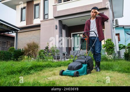 uomo stanco che usa un rasaerba tagliando l'erba a casa Foto Stock