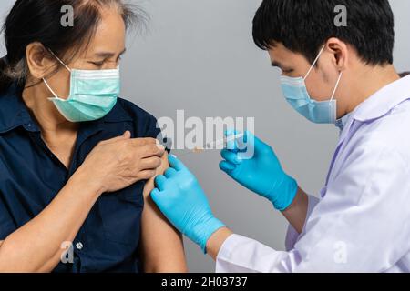 medico che tiene la siringa e usando il cotone prima di fare l'iniezione alla donna in una maschera medica. Covid-19 o vaccino contro il coronavirus Foto Stock