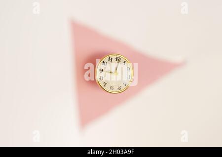 Orologio vintage in un triangolo bianco sfocato su sfondo rosa. Orologio da tavolo rotondo meccanico in telaio dorato. Messa a fuoco selettiva. Foto Stock