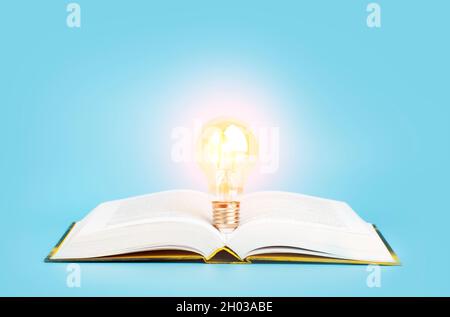 Concetto di apprendimento dello studio della conoscenza. Apri un libro con una lampadina luminosa su sfondo blu. Ricerca, lettura e studio dell'idea. Foto di alta qualità Foto Stock