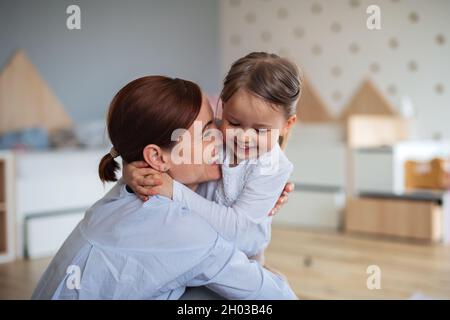 Felice madre con la piccola figlia che abbraccia in camera da letto, ridendo. Foto Stock