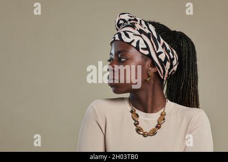 Ritratto minimal vista laterale della giovane donna afroamericana che guarda via indossando accessori etnici e posando su sfondo beige marrone neutro, spazio copia Foto Stock