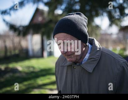 Ritratto di uomo anziano in giacca e con cappello a maglia che cammina nella giornata invernale di sole Foto Stock