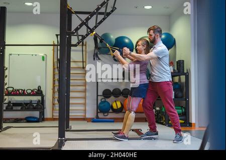 Personal trainer che assiste la donna con disabilità nel suo allenamento Foto Stock