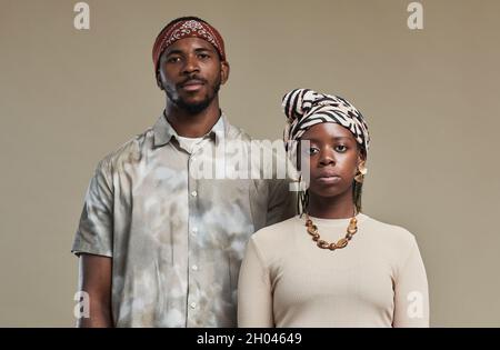Ritratto in vita di coppia contemporanea afroamericana che indossa le pellicole per la testa e guarda la fotocamera mentre si trova su sfondo beige neutro in studio Foto Stock