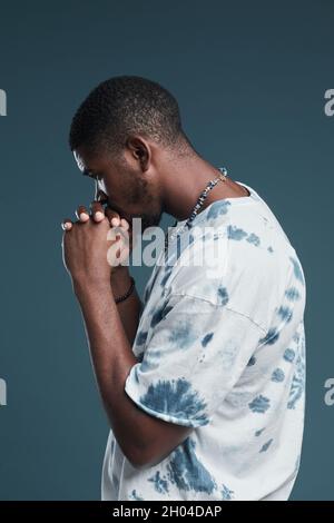 Ritratto verticale laterale del giovane uomo afroamericano che indossa abiti casual da strada mentre si posa contro il blu Foto Stock
