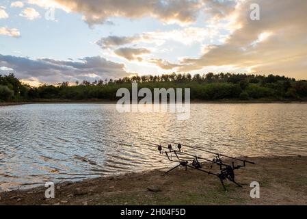 Avventure di pesca, pesca carpe. Il pescatore, al tramonto, è la pesca con la tecnica del carpfishing. Campeggio sulla riva del lago. Carp pesca Tramonto. Foto Stock