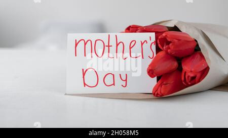 Giornata delle madri. Un bouquet di tulipani rossi e una tessera con l'iscrizione Festa della mamma su sfondo bianco. Fiori in carta artigianale. Consegna fiori Foto Stock