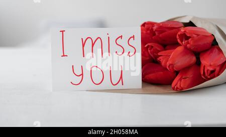 Fiori a una donna. Bouquet di tulipani rossi e biglietto d'auguri con iscrizione manoscritta mi manchi su sfondo bianco. Consegna fiori Foto Stock