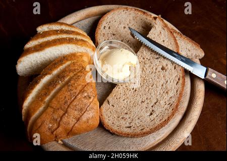 Pane di grano intero appena sfornato e burro su un piatto di legno Foto Stock