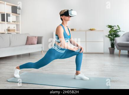 App VR Workout, gioco di fitness. Le cuffie sportive per la realtà vrtuale si esercitano utilizzando l'applicazione digitale, facendo il forward lunges a casa. Donna che usa m Foto Stock