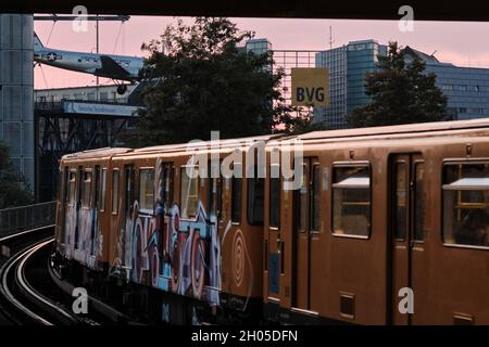 Berlino, Germania. 10 Ott 2021. Una metropolitana del Berliner Verkehrsbetriebe (BVG) corre sulla linea elevata dalla stazione della metropolitana Möckernbrücke nel distretto Kreuzberg verso il Museo tedesco della tecnologia sul cui tetto si trova un aereo Douglas C-47, chiamato 'raisin bombardiere'. Sullo sfondo, un edificio per uffici con un grande cartello BVG può essere visto sulla destra. Credit: Stefan Jaitner/dpa/Alamy Live News Foto Stock