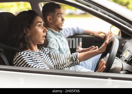 Giovane pilota stordito che guarda la strada con espressione del volto scioccato, che ha un giro in auto con partner uomo millenario medio-orientale, vista laterale, auto c Foto Stock